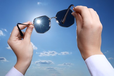 Photo of Woman holding funny sunglasses against blue sky on sunny day, low angle view