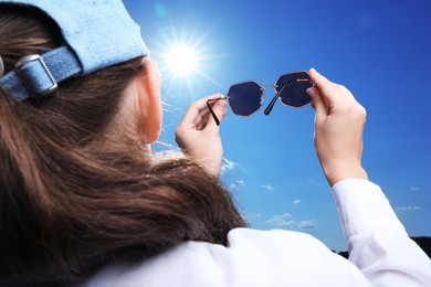 Photo of Woman holding funny sunglasses against blue sky on sunny day, low angle view