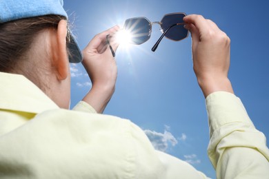 Photo of Woman holding funny sunglasses against blue sky on sunny day, low angle view