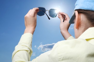 Photo of Woman holding funny sunglasses against blue sky on sunny day, low angle view