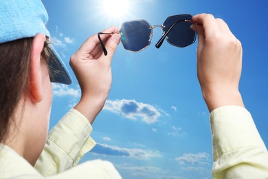 Photo of Woman holding funny sunglasses against blue sky on sunny day, low angle view