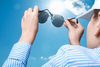 Photo of Woman holding funny sunglasses against blue sky on sunny day, low angle view