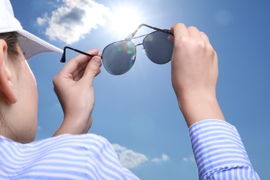 Photo of Woman holding funny sunglasses against blue sky on sunny day, low angle view