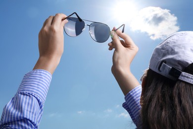 Photo of Woman holding funny sunglasses against blue sky on sunny day, low angle view