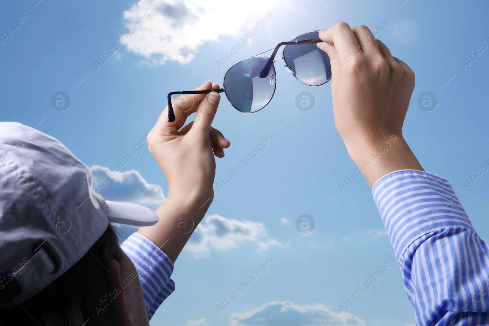 Photo of Woman holding funny sunglasses against blue sky on sunny day, low angle view