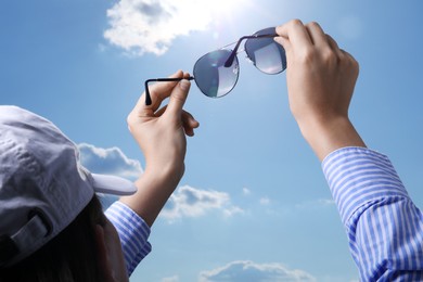 Photo of Woman holding funny sunglasses against blue sky on sunny day, low angle view