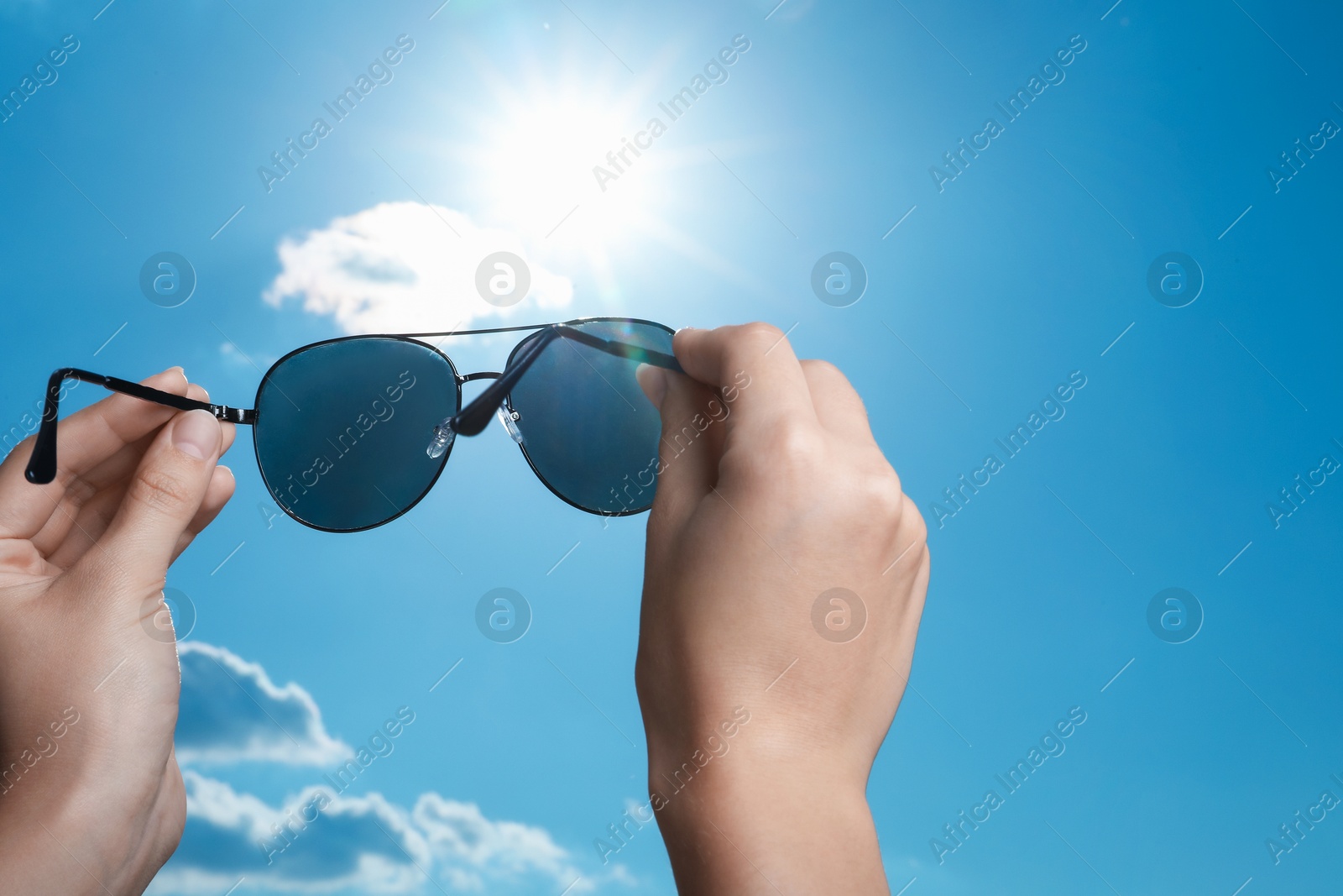 Photo of Woman holding funny sunglasses against blue sky on sunny day, low angle view. Space for text