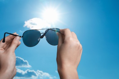 Photo of Woman holding funny sunglasses against blue sky on sunny day, low angle view. Space for text
