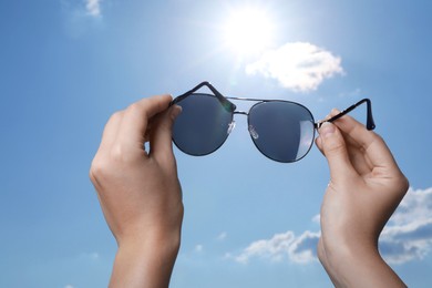 Photo of Woman holding funny sunglasses against blue sky on sunny day, low angle view