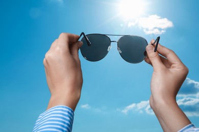 Photo of Woman holding funny sunglasses against blue sky on sunny day, low angle view