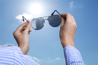 Photo of Woman holding funny sunglasses against blue sky on sunny day, low angle view