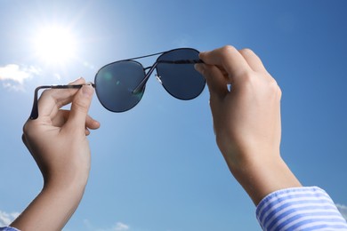 Photo of Woman holding funny sunglasses against blue sky on sunny day, low angle view