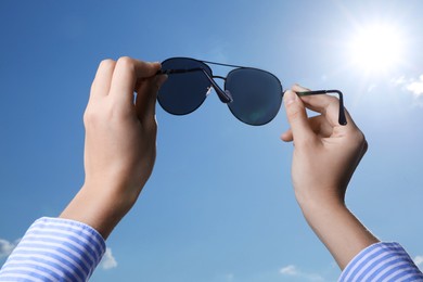 Photo of Woman holding funny sunglasses against blue sky on sunny day, low angle view