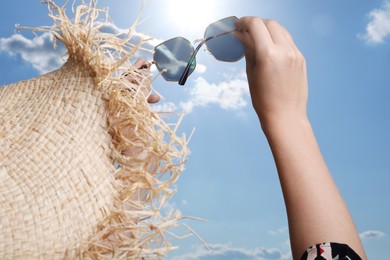 Photo of Woman holding funny sunglasses against blue sky on sunny day, low angle view
