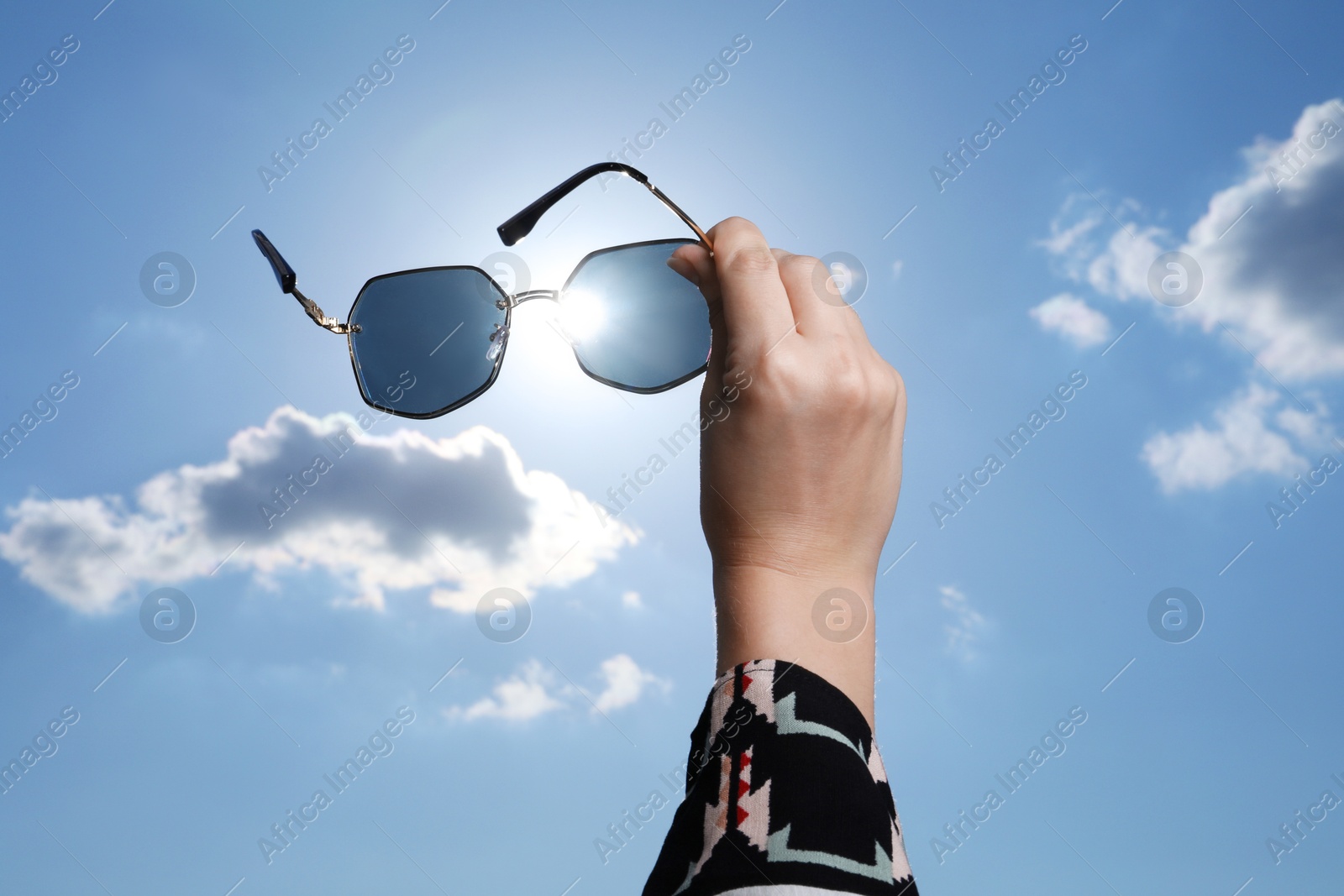 Photo of Woman holding funny sunglasses against blue sky on sunny day, low angle view