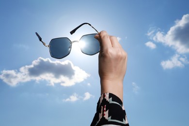 Photo of Woman holding funny sunglasses against blue sky on sunny day, low angle view