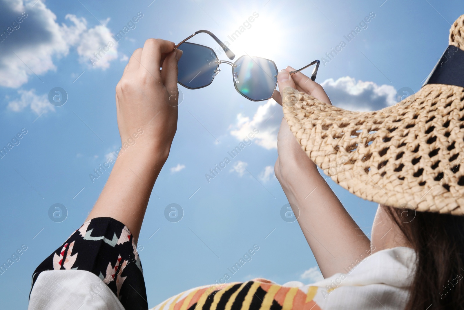 Photo of Woman holding funny sunglasses against blue sky on sunny day, low angle view