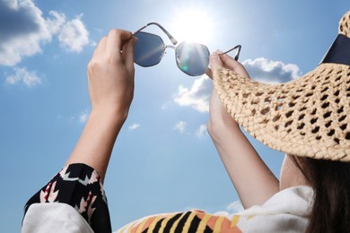 Photo of Woman holding funny sunglasses against blue sky on sunny day, low angle view