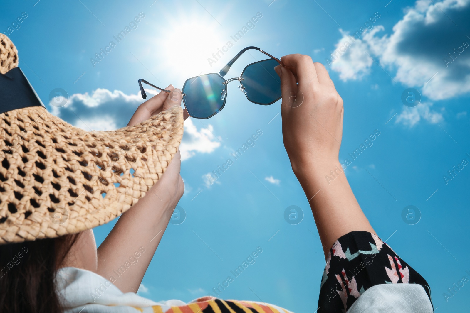 Photo of Woman holding funny sunglasses against blue sky on sunny day, low angle view