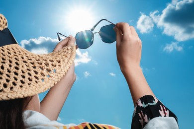 Photo of Woman holding funny sunglasses against blue sky on sunny day, low angle view