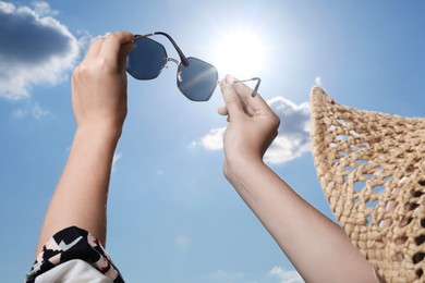 Photo of Woman holding funny sunglasses against blue sky on sunny day, low angle view