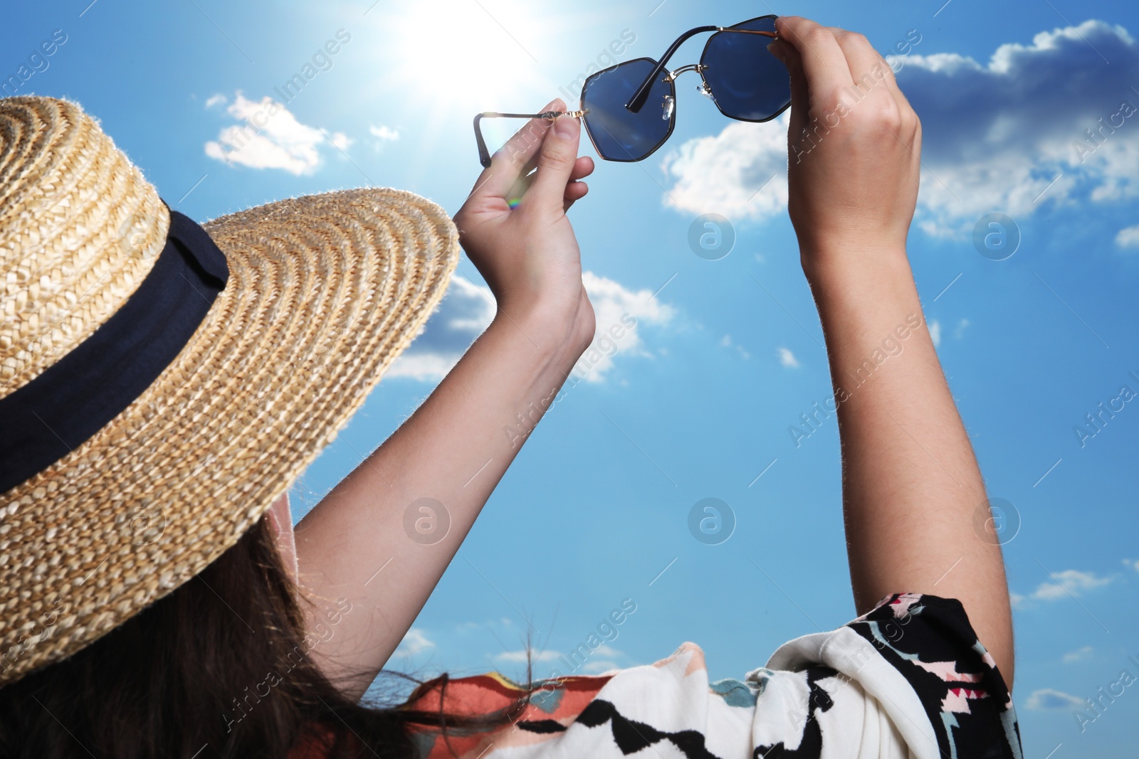 Photo of Woman holding funny sunglasses against blue sky on sunny day, low angle view