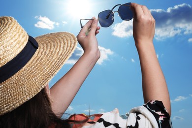 Photo of Woman holding funny sunglasses against blue sky on sunny day, low angle view