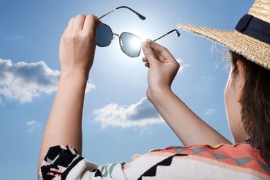 Photo of Woman holding funny sunglasses against blue sky on sunny day, low angle view