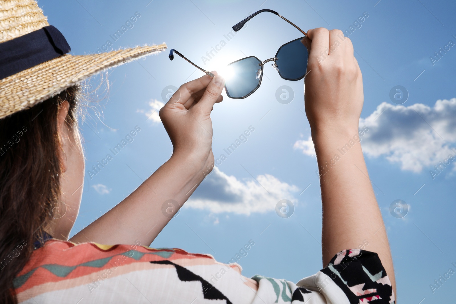 Photo of Woman holding funny sunglasses against blue sky on sunny day, low angle view