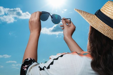 Photo of Woman holding funny sunglasses against blue sky on sunny day, low angle view