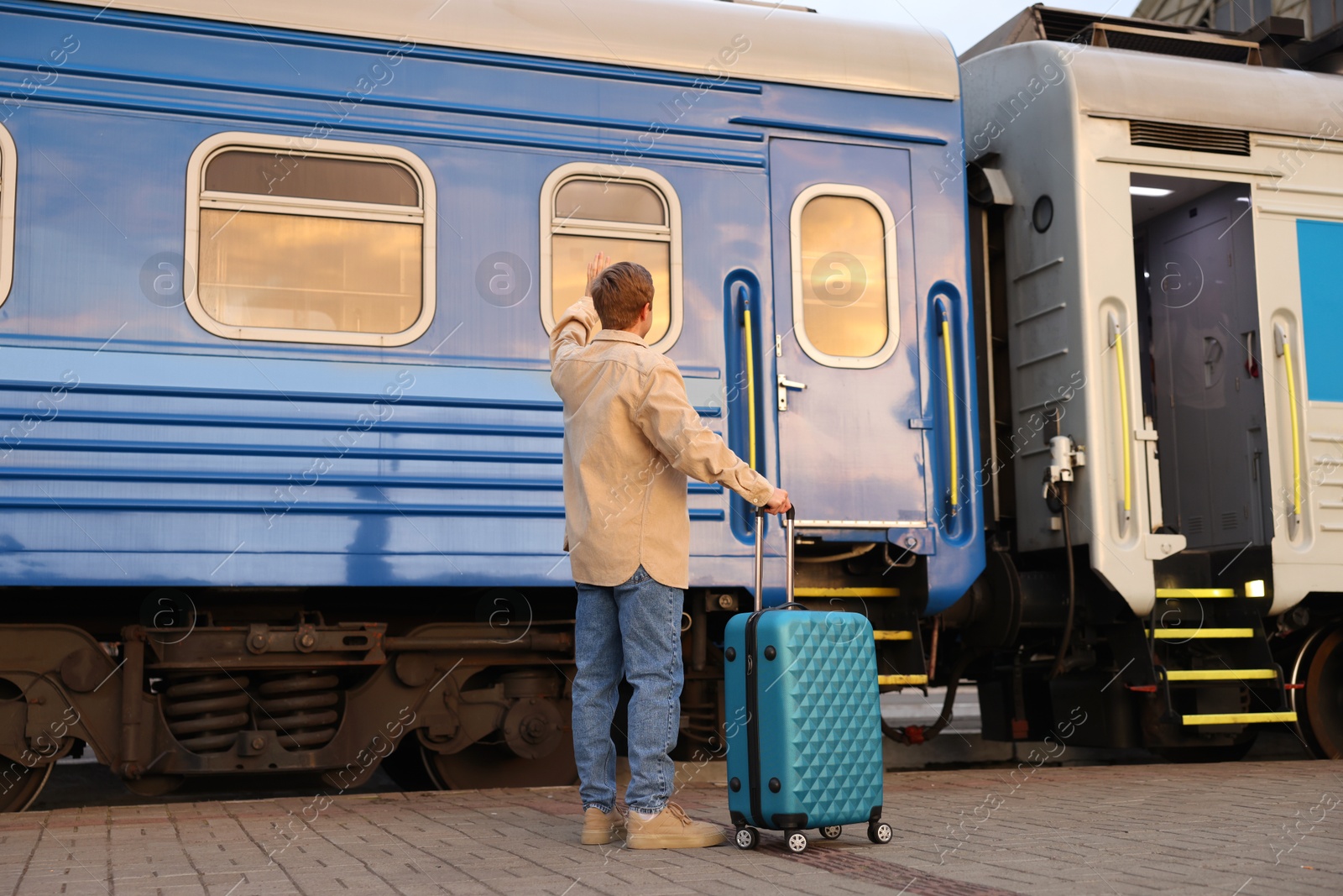 Photo of Goodbye. Man with luggage waving near train outdoors, back view