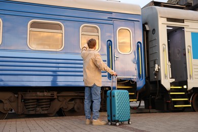 Photo of Goodbye. Man with luggage waving near train outdoors, back view