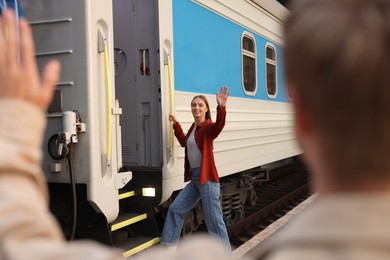 Photo of Goodbye. Man waving to his girlfriend near train outdoors, selective focus
