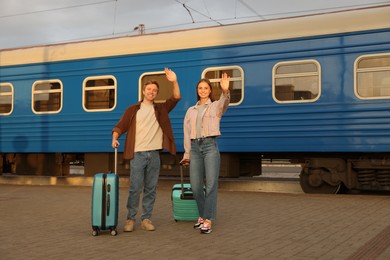 Photo of Goodbye. Couple with suitcases waving on platform of railway station
