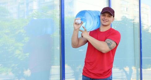 Photo of Smiling delivery man with cooler bottle of water near building outdoors. Space for text