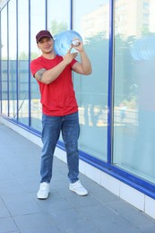 Photo of Smiling delivery man with cooler bottle of water near building outdoors