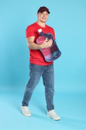 Photo of Smiling delivery man with cooler bottle of water on light blue background