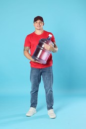 Photo of Smiling delivery man with cooler bottle of water on light blue background