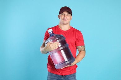 Photo of Smiling delivery man with cooler bottle of water on light blue background