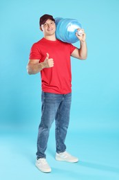 Photo of Smiling delivery man with cooler bottle of water showing thumbs up on light blue background