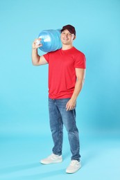 Photo of Smiling delivery man with cooler bottle of water on light blue background