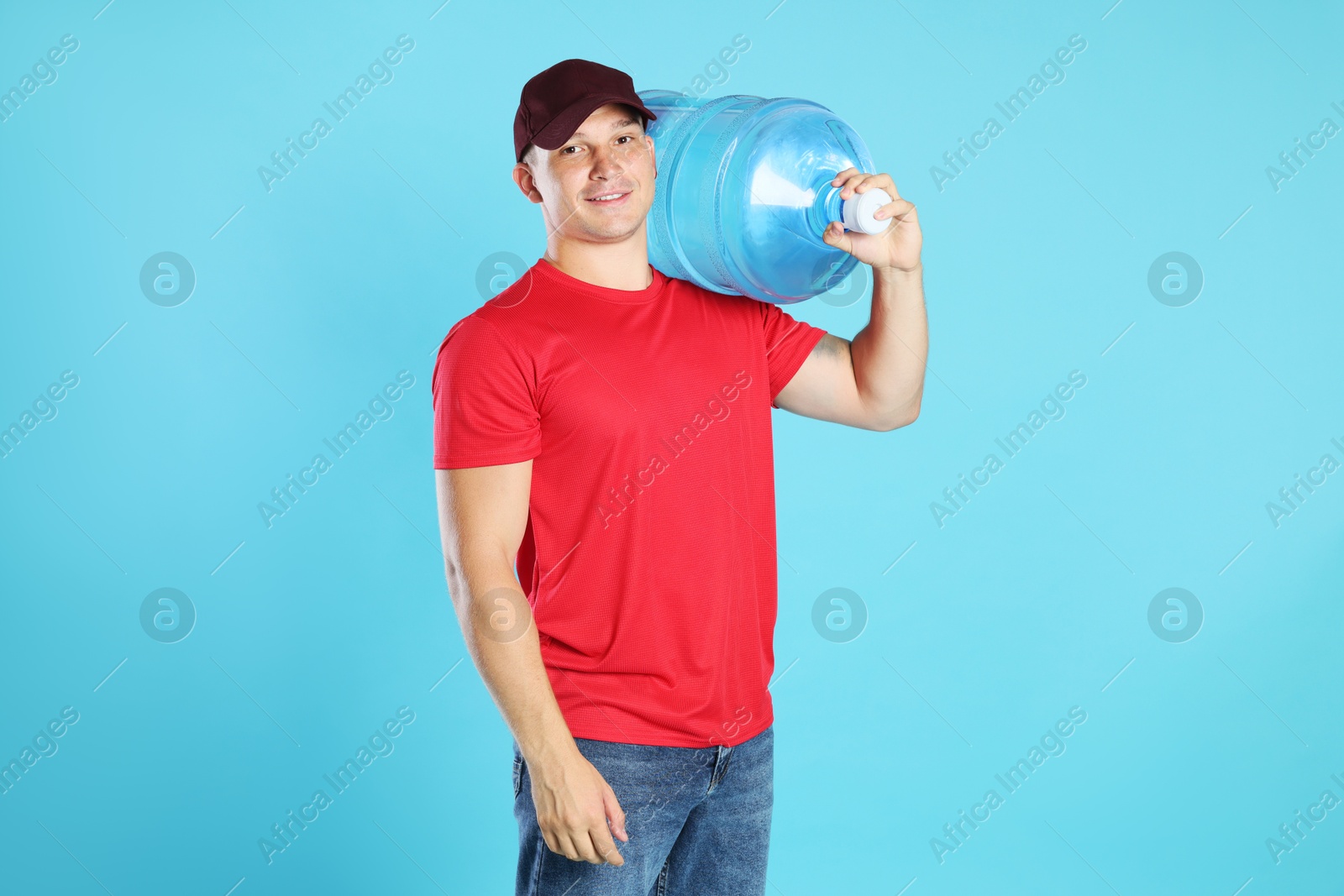 Photo of Smiling delivery man with cooler bottle of water on light blue background