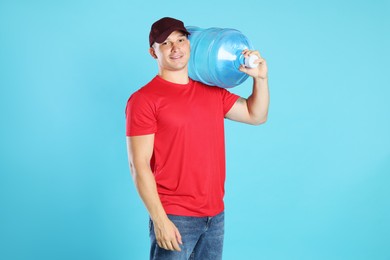 Photo of Smiling delivery man with cooler bottle of water on light blue background