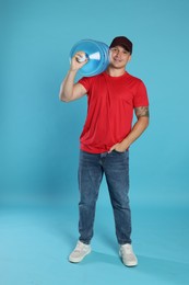 Photo of Smiling delivery man with cooler bottle of water on light blue background