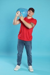 Photo of Smiling delivery man with cooler bottle of water on light blue background