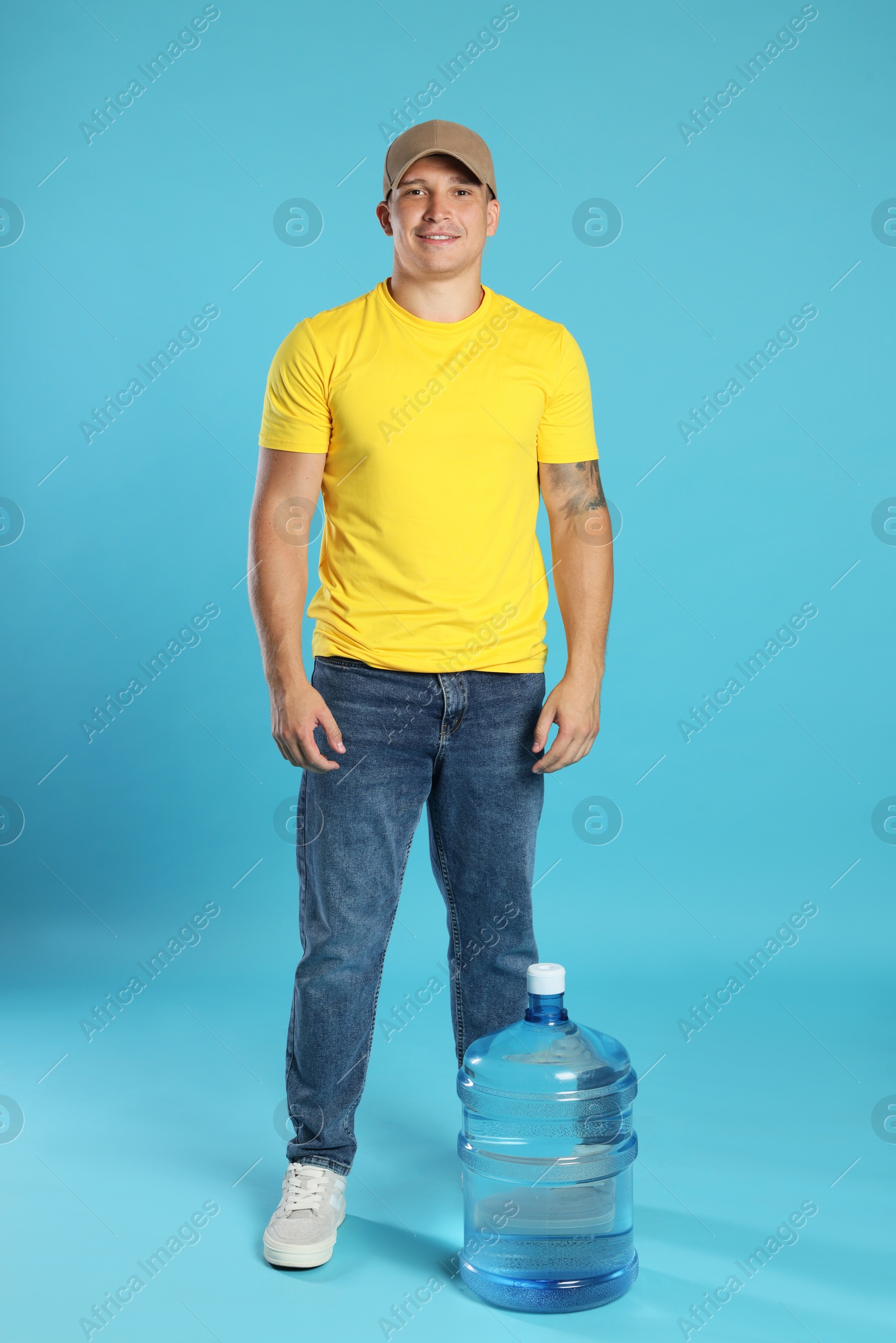 Photo of Smiling delivery man and cooler bottle of water on light blue background