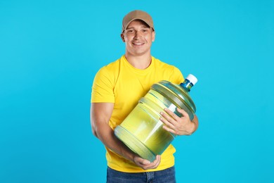 Photo of Smiling delivery man with cooler bottle of water on light blue background