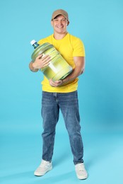 Photo of Smiling delivery man with cooler bottle of water on light blue background