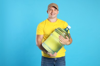 Photo of Smiling delivery man with cooler bottle of water on light blue background