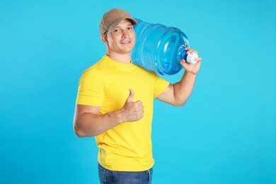 Photo of Smiling delivery man with cooler bottle of water showing thumbs up on light blue background